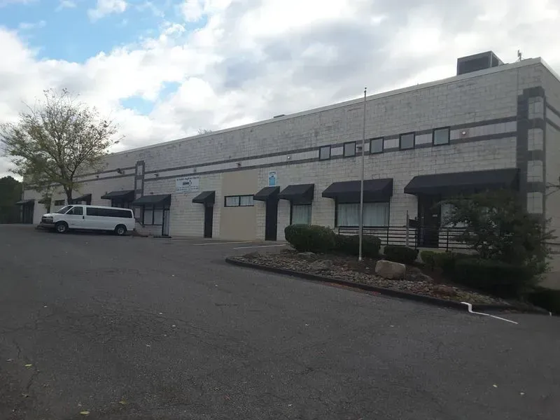 A long, light-colored brick building with black awnings, a white van parked in front, and a cloudy sky.