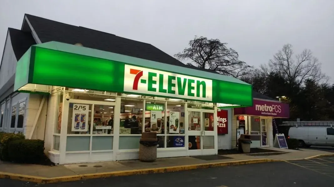 7-Eleven convenience store with green and white signage, lit up at dusk. Next door is a Metro by T-Mobile store.
