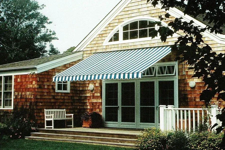 Blue and white striped awning over French doors of a cedar-shingled house.