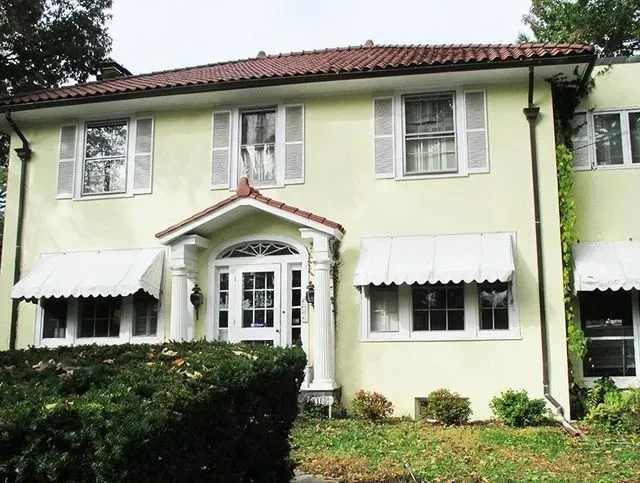 Yellow two-story house with white shutters, awnings, and a red tile roof.