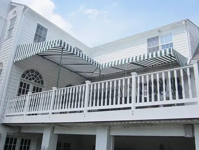 White house with a green and white striped awning over a porch with a white railing.