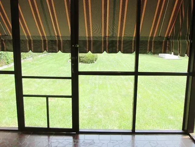 View from a screened porch: green lawn and shrubbery outside; awning overhead.