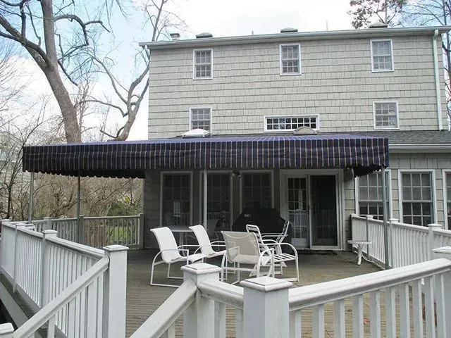 Two-story house with a wooden deck and a black awning over a patio.
