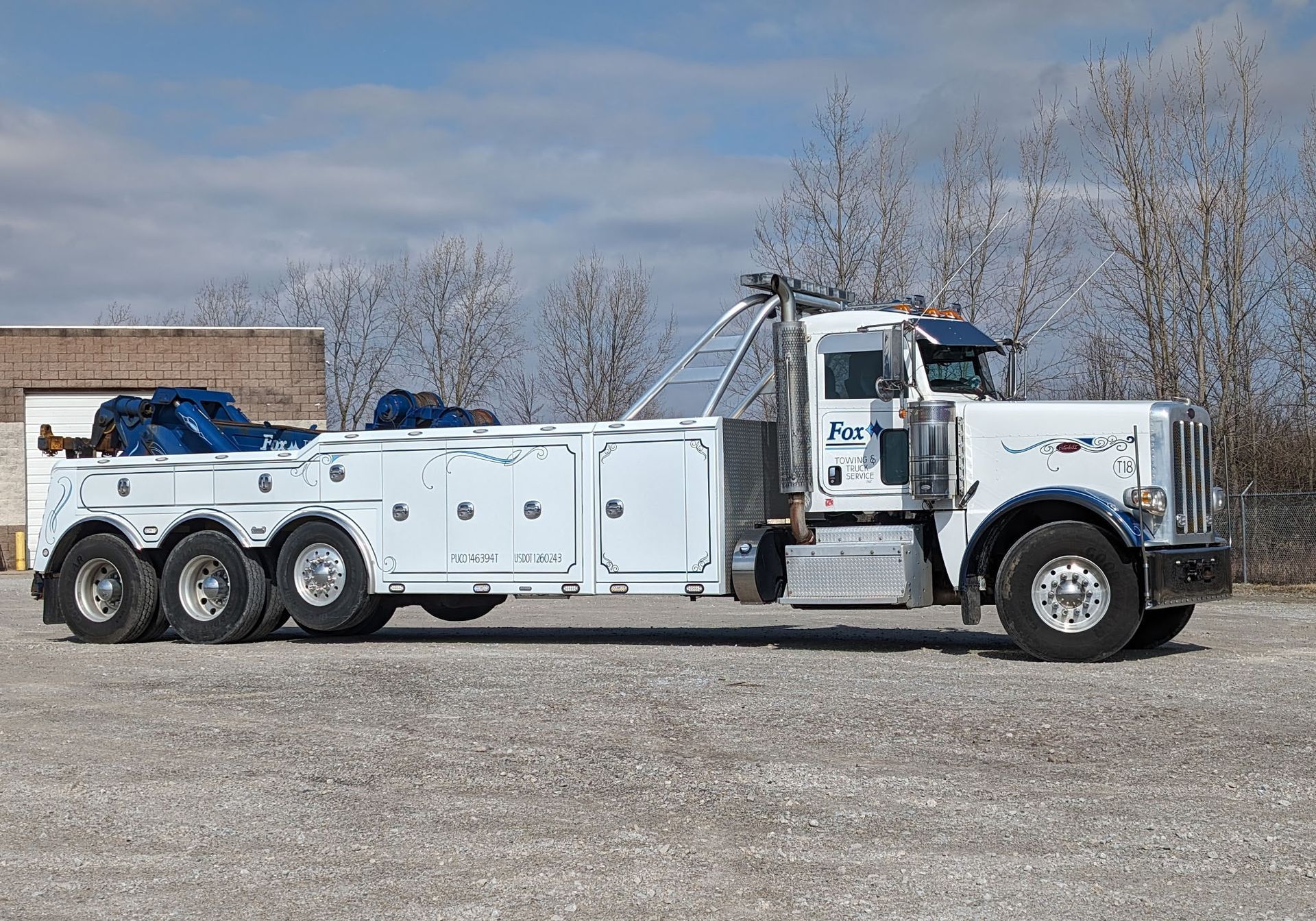 White tow truck parked on gravel, under a partly cloudy sky.
