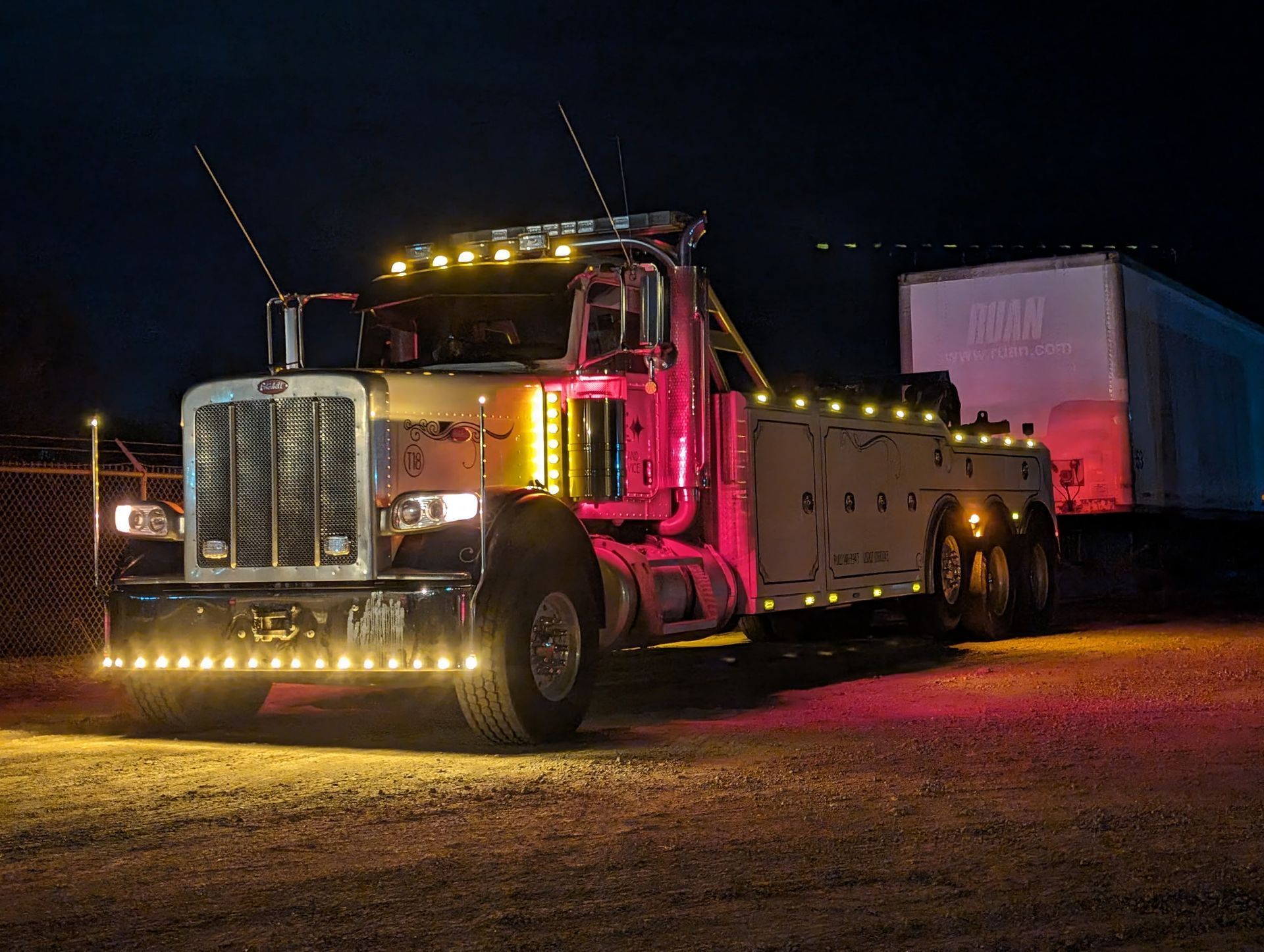 Illuminated tow truck at night towing a semi-trailer.