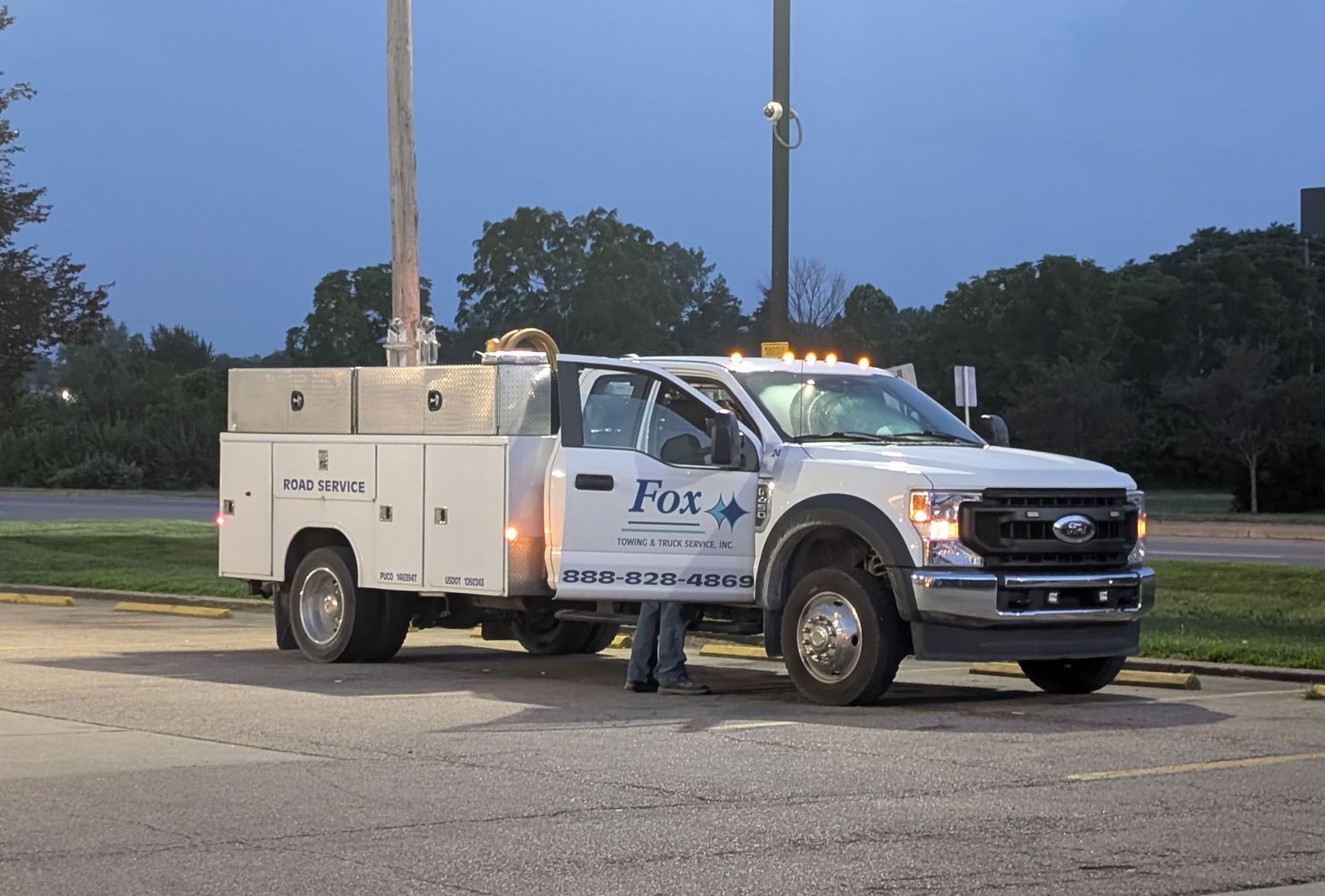 White work truck with open door; person standing by the door, nighttime scene; Fix logo.