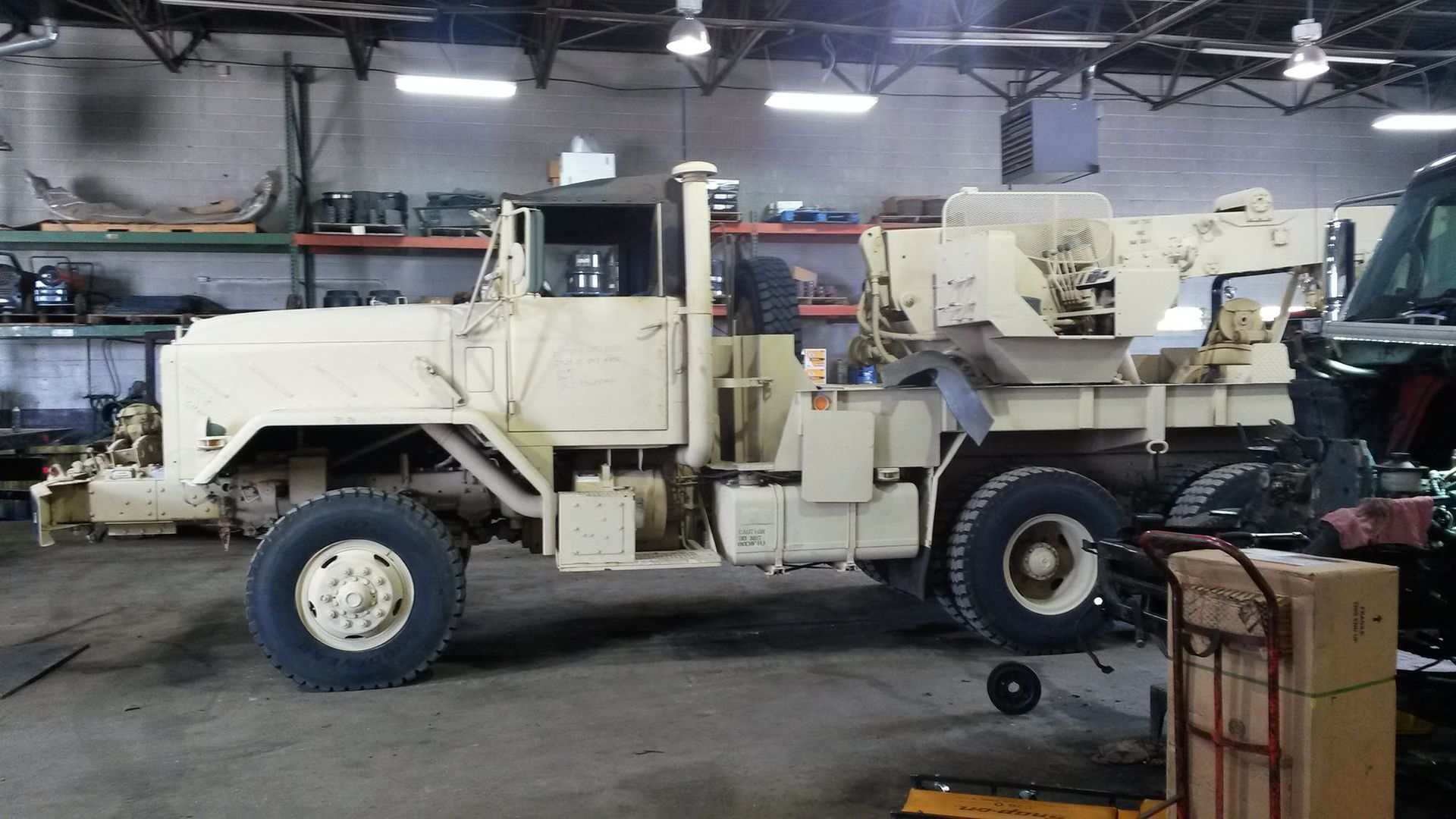 Tan military truck in a workshop with mechanical components visible.