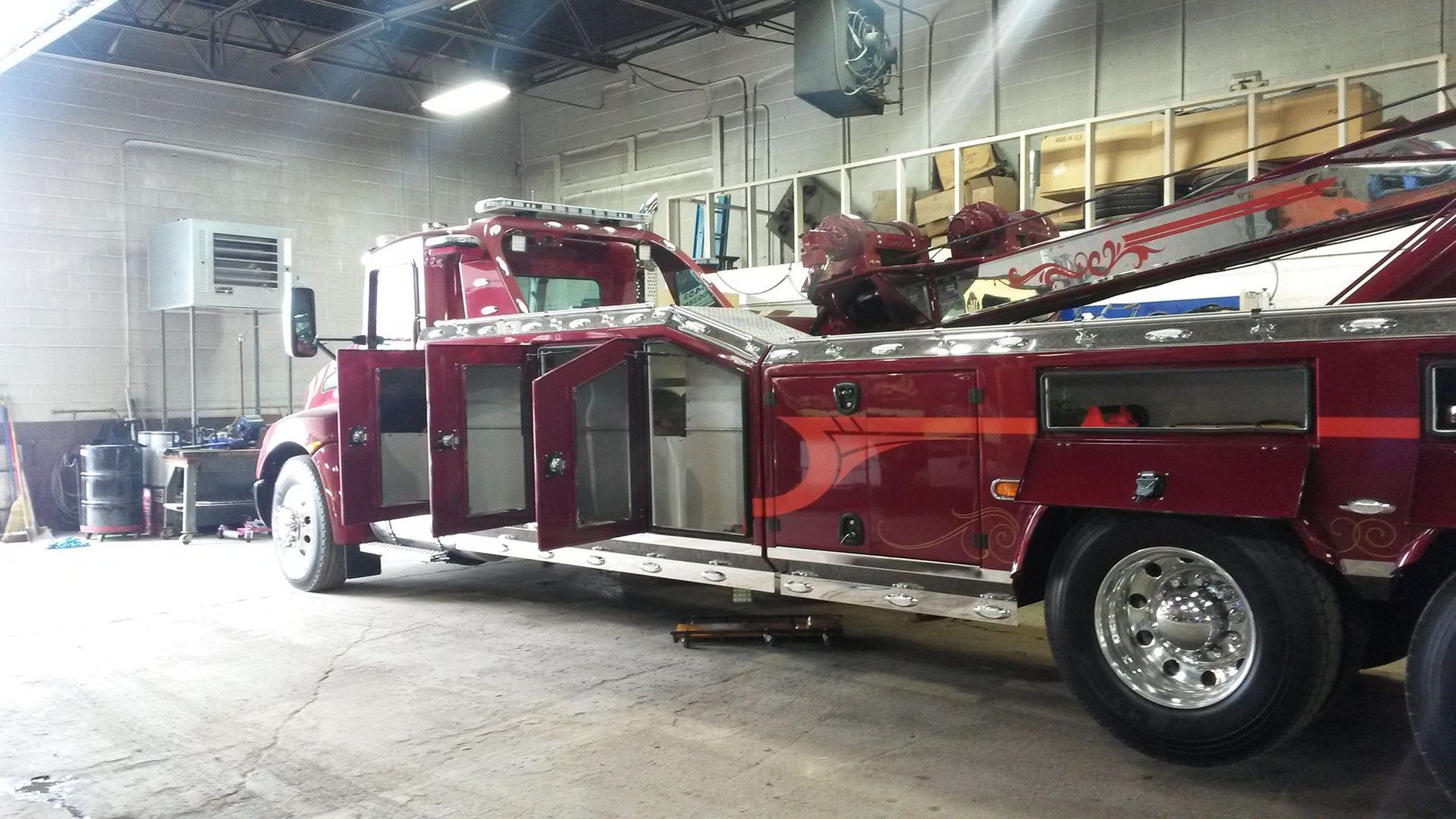 A maroon tow truck with open doors inside a garage.