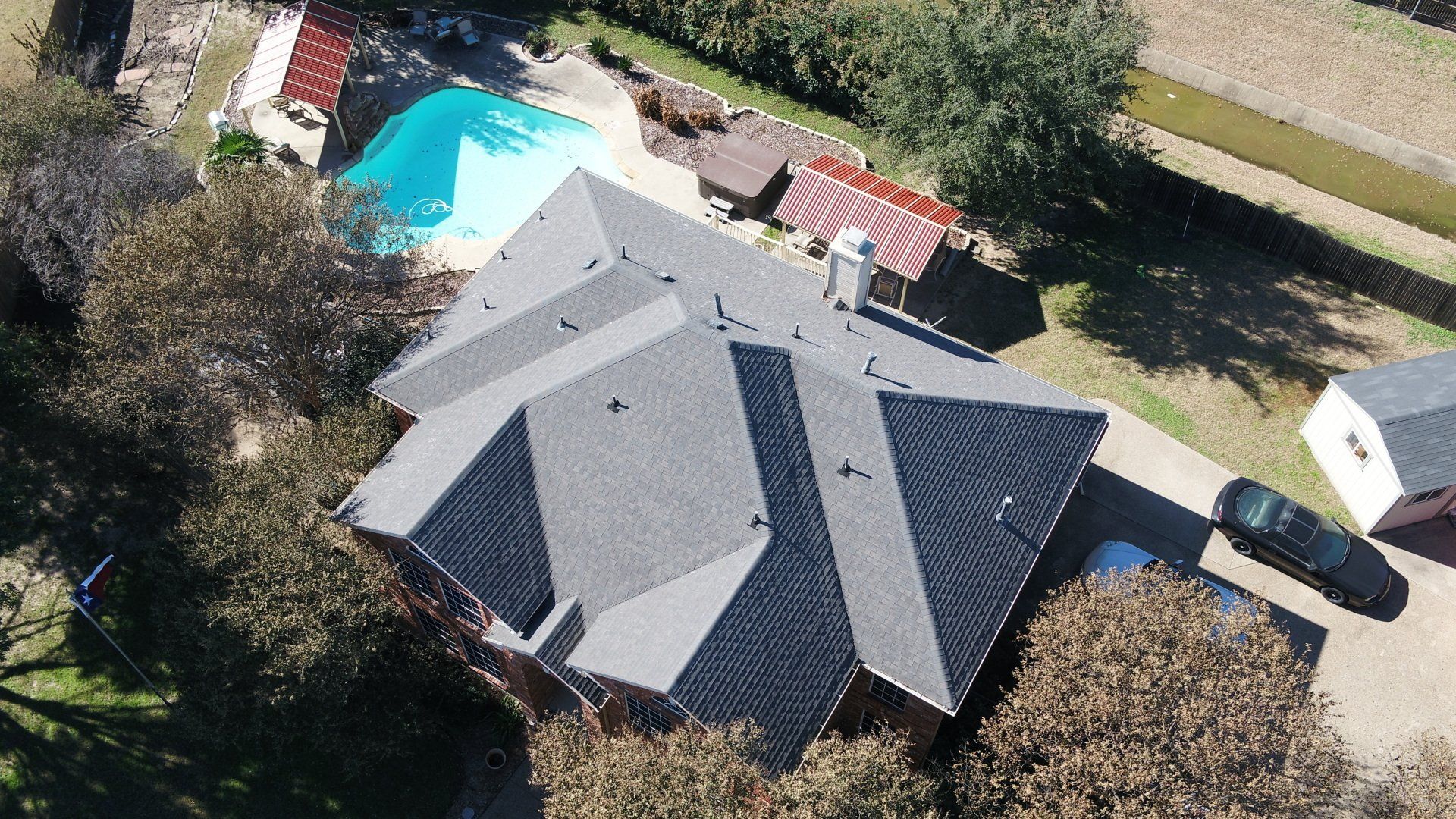 Overhead view of a house with gray roof, swimming pool, and car parked in driveway.