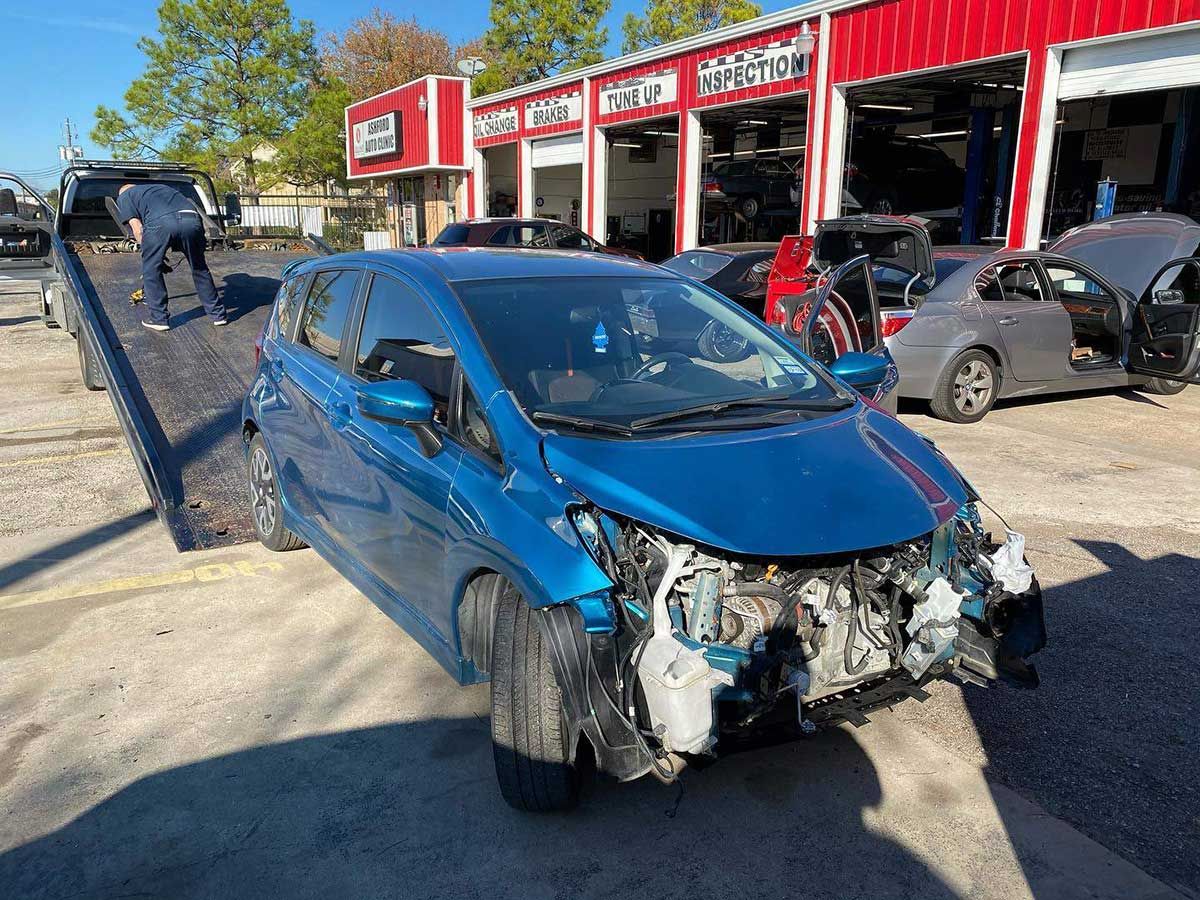 A blue car is sitting on top of a tow truck in front of a garage.