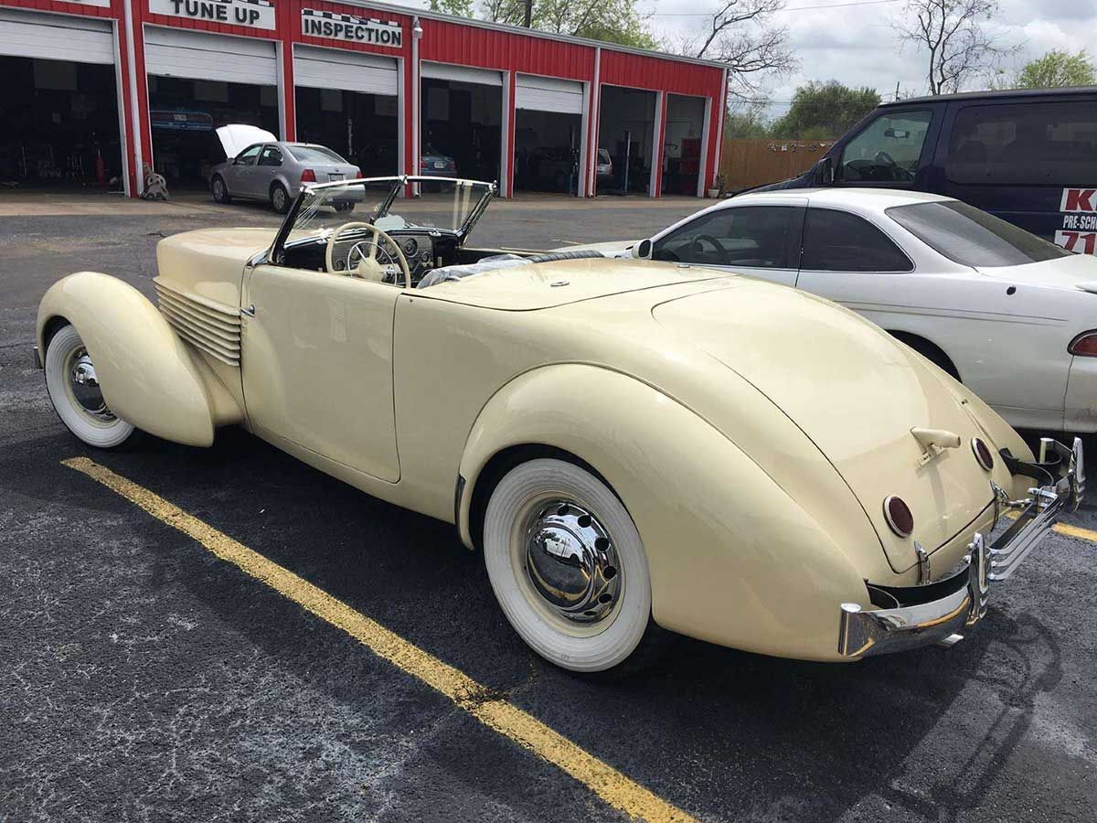 A white car is parked in a parking lot in front of a garage.