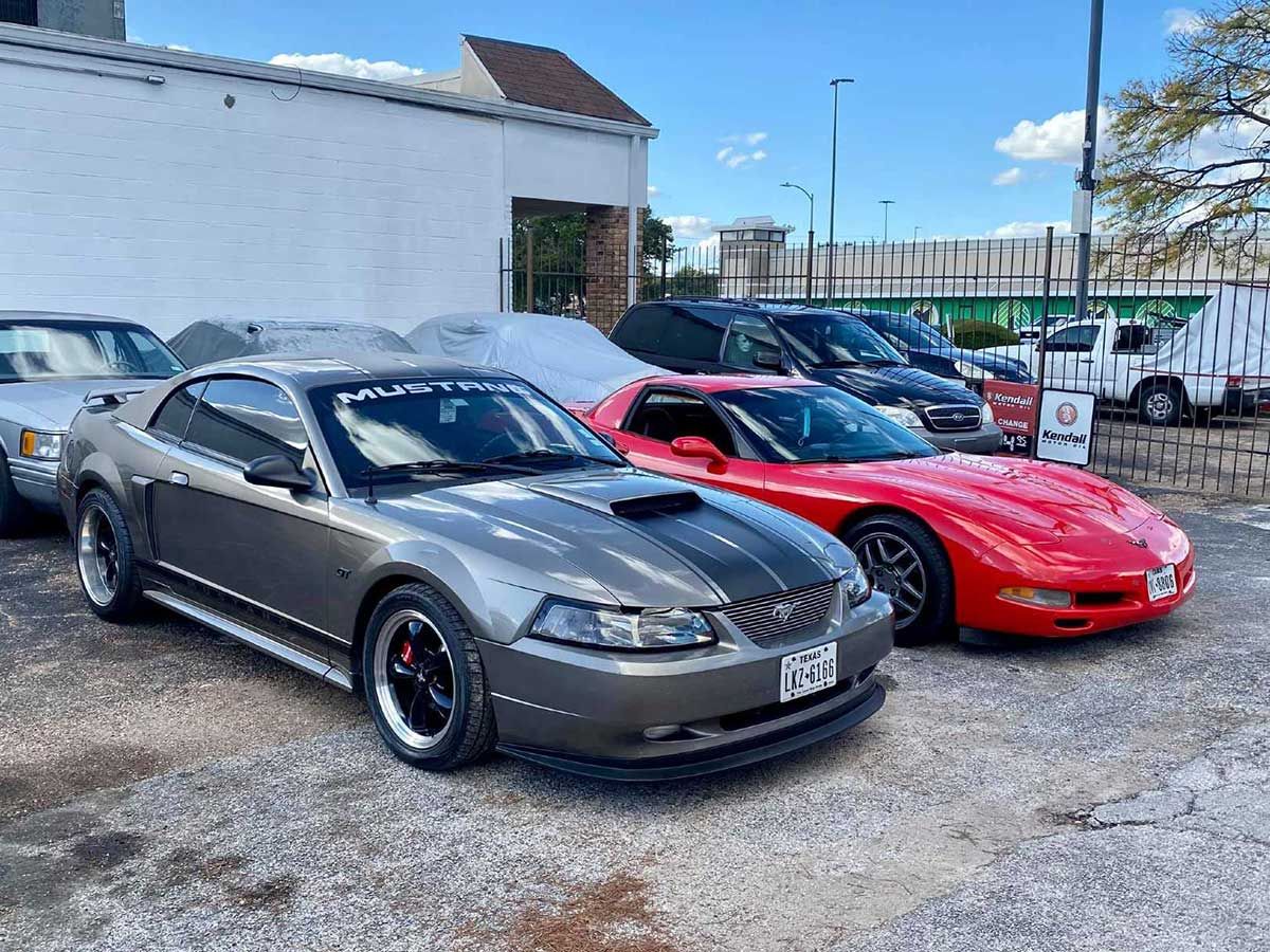 A gray mustang and a red corvette are parked next to each other in a parking lot.