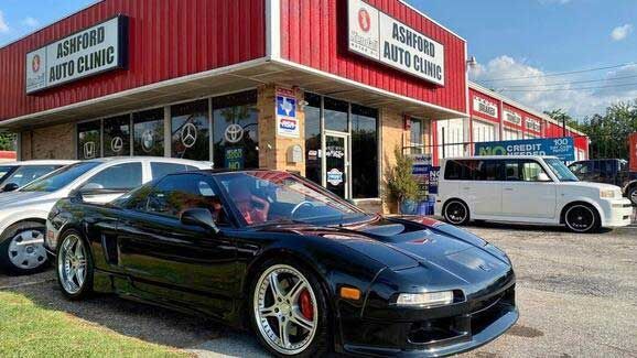 A black sports car is parked in front of a car dealership.