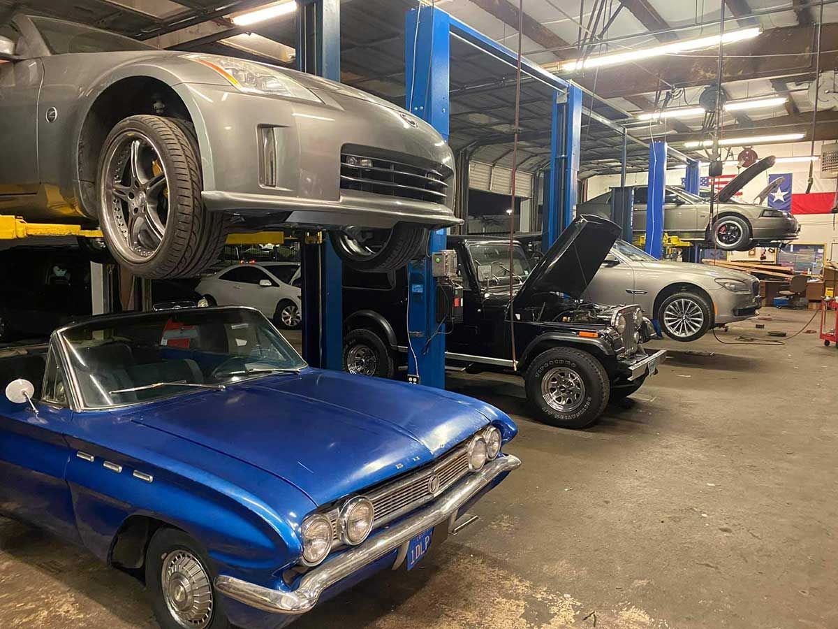 A blue car is parked in a garage next to a gray car on a lift.
