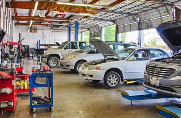 A row of cars are parked in a garage with their hoods open.