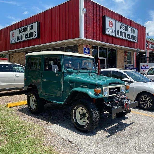 A green jeep is parked in front of an ashford auto clinic