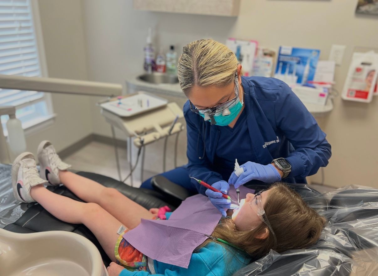 A dentist examining a child's teeth in a dental chair.
