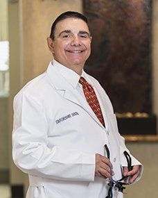 Construction worker with red hard hat smiles, arms crossed, at desk with blueprints and laptop.