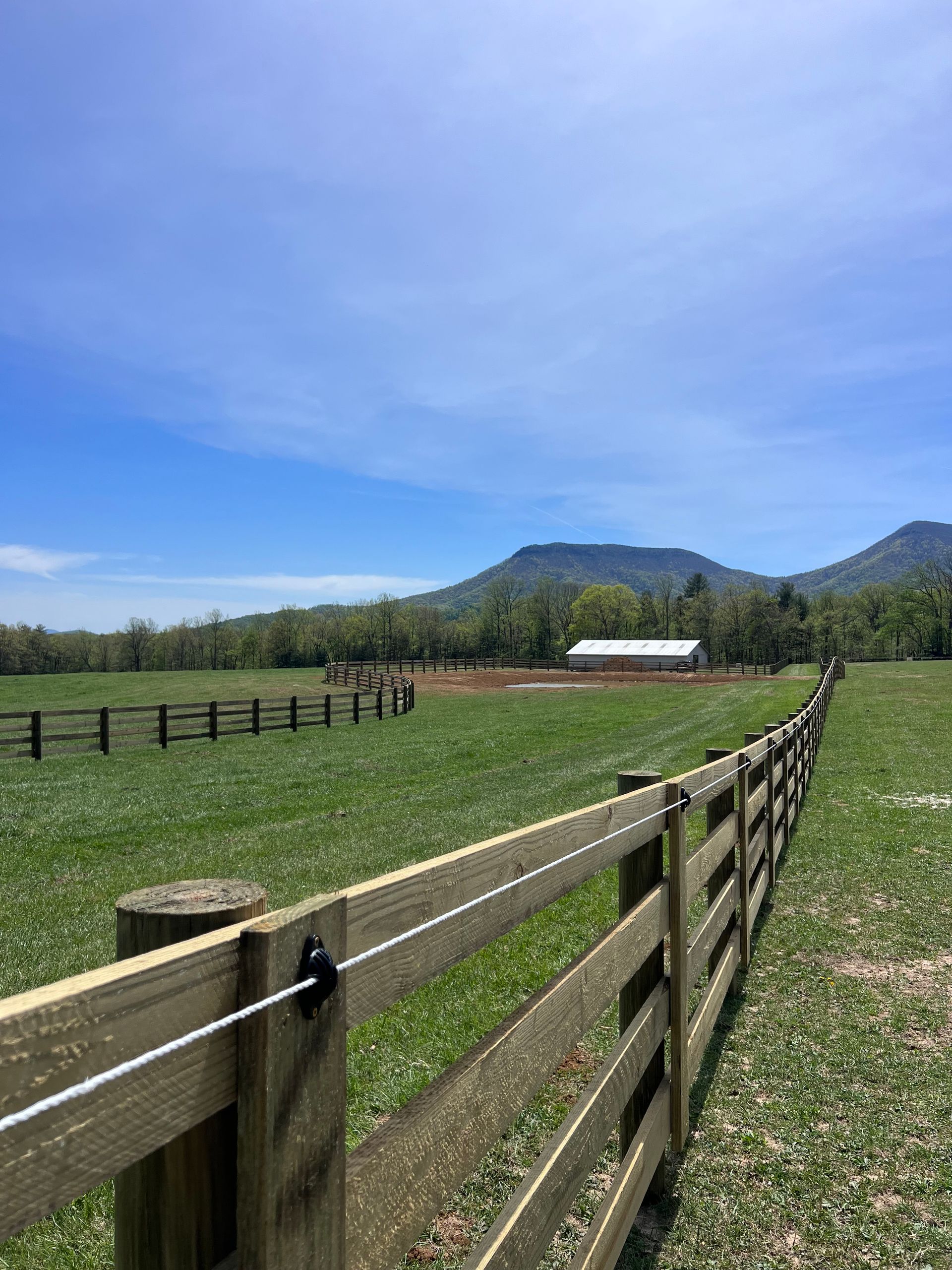 A wooden fence surrounds a grassy field with mountains in the background.