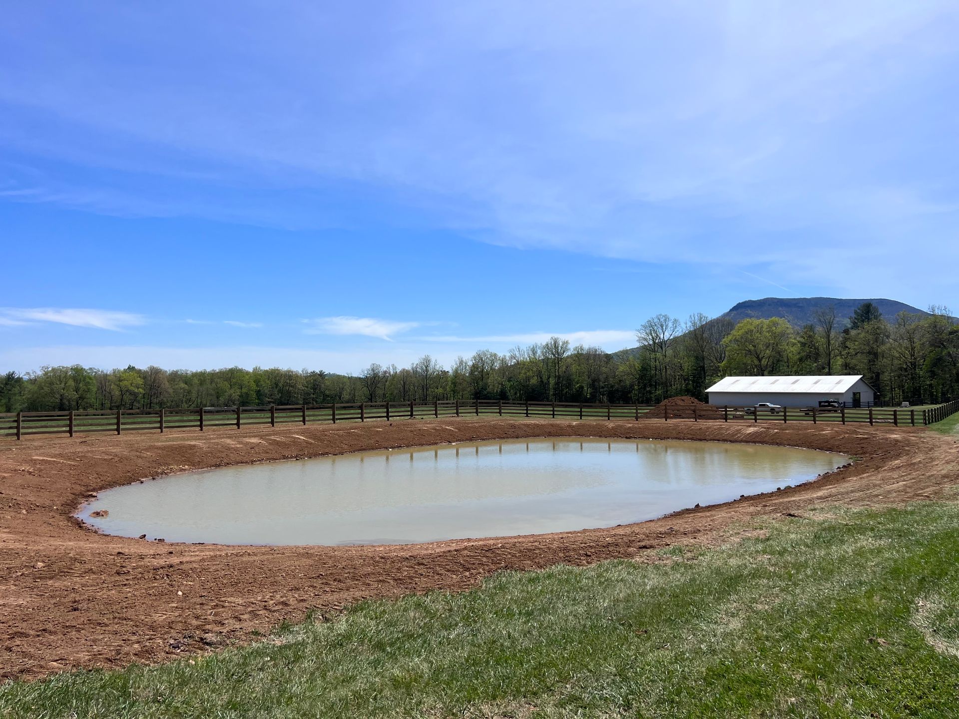 A small pond in the middle of a field with a barn in the background.