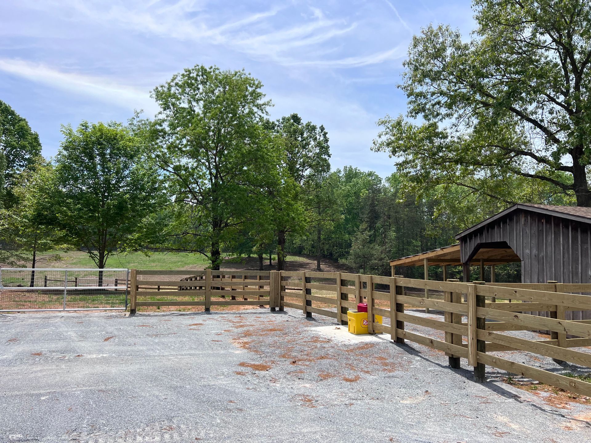 A wooden fence surrounds a gravel area with trees in the background.