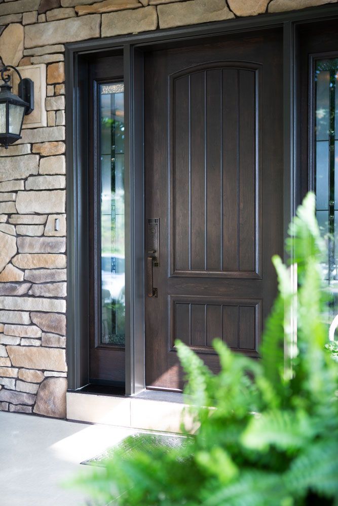 The front door of a house with a stone wall and a fern in front of it.