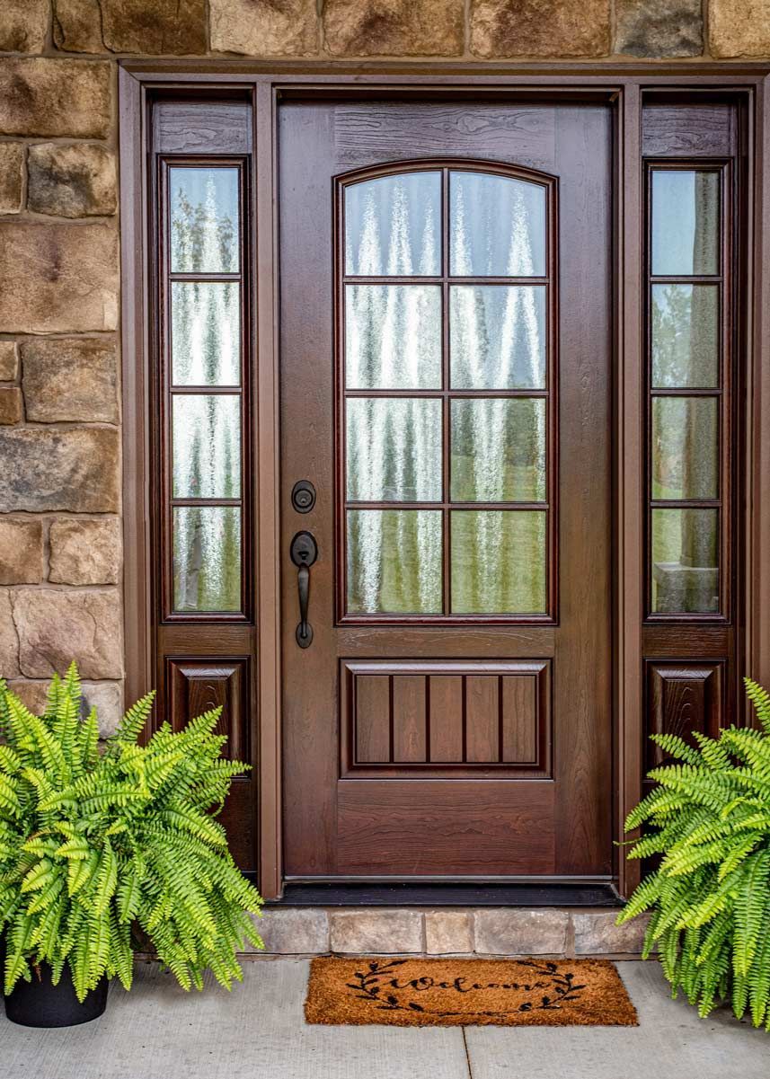 A wooden door with ferns in front of it and a welcome mat.