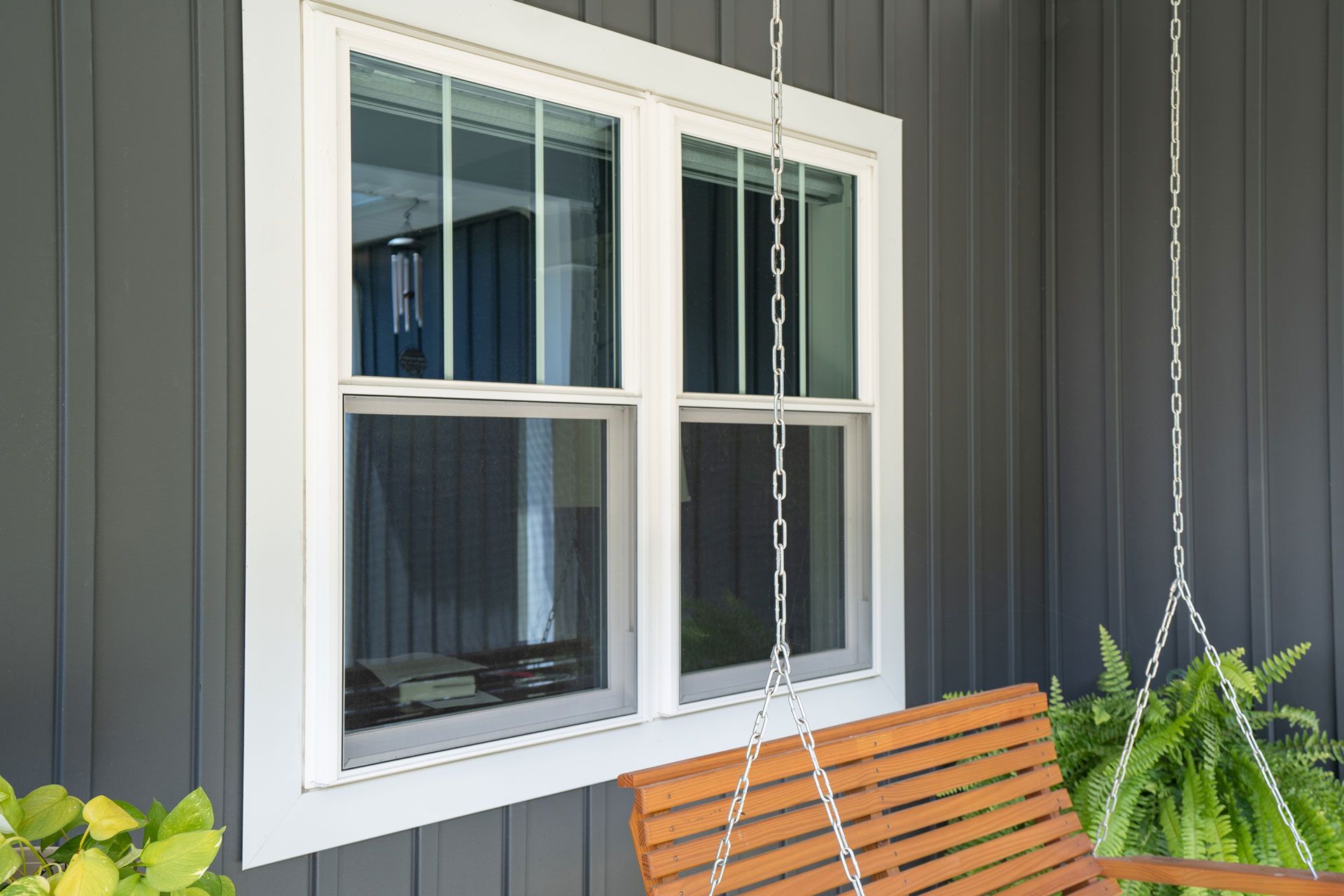 A porch swing is hanging from chains in front of a window.