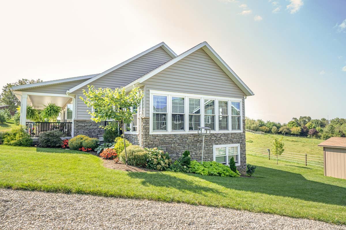 A house with a lot of windows is sitting on top of a lush green hill.