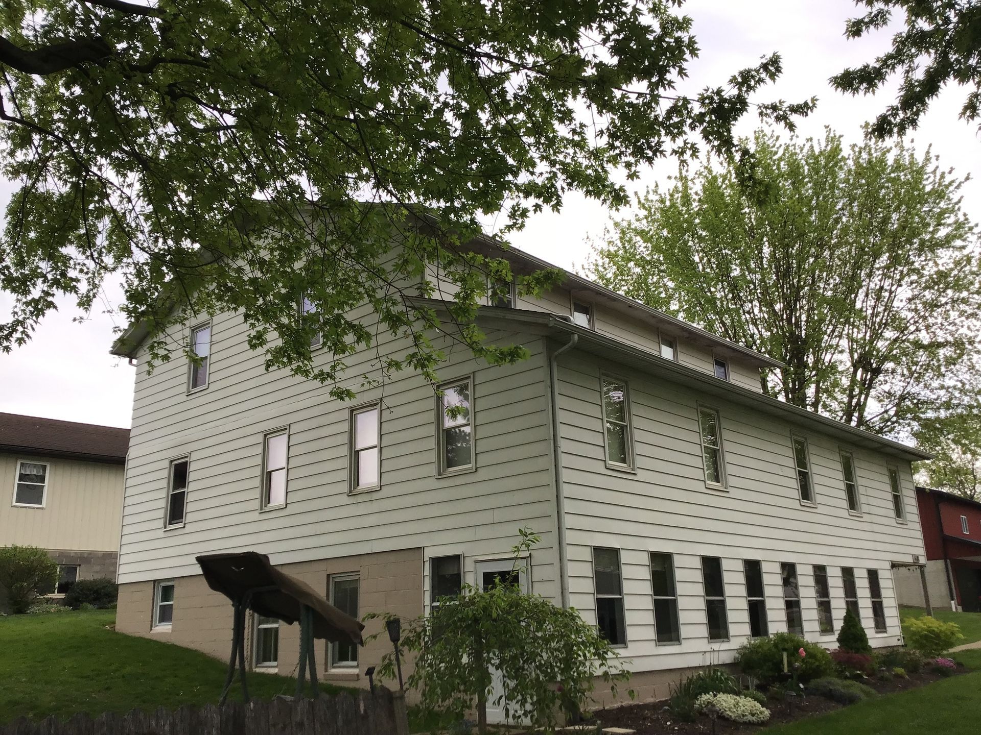 white siding house with lower patio and trees
