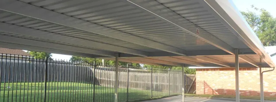 Covered parking area with metal roof, black fence, and red brick building in the background