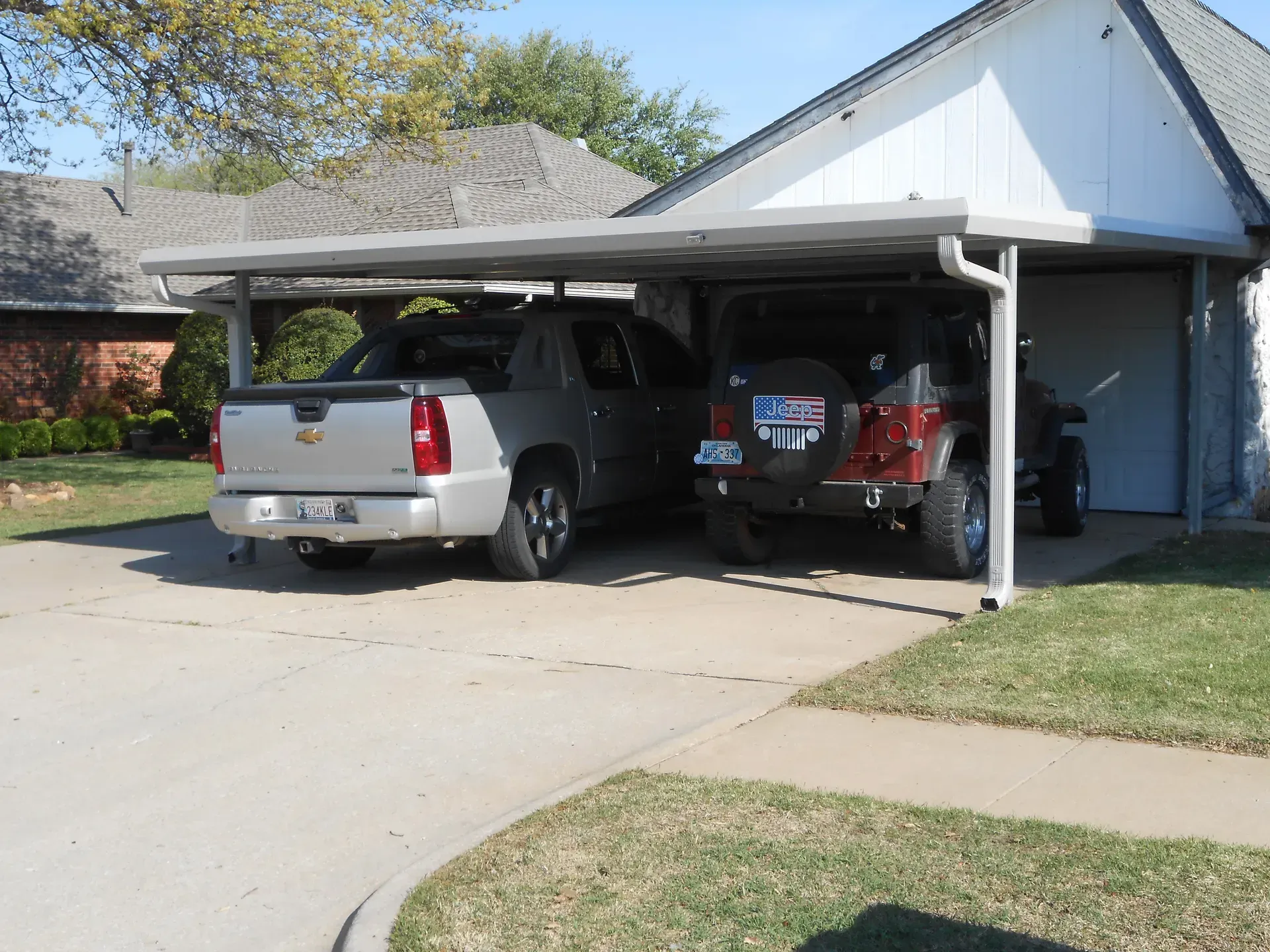 Two pickup trucks parked side by side under a white carport at a suburban house