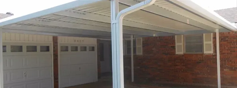 Carport attached to a brick house with white support posts and a double garage door