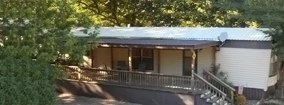 Small beige house with a covered porch, front stairs, and trees in the yard