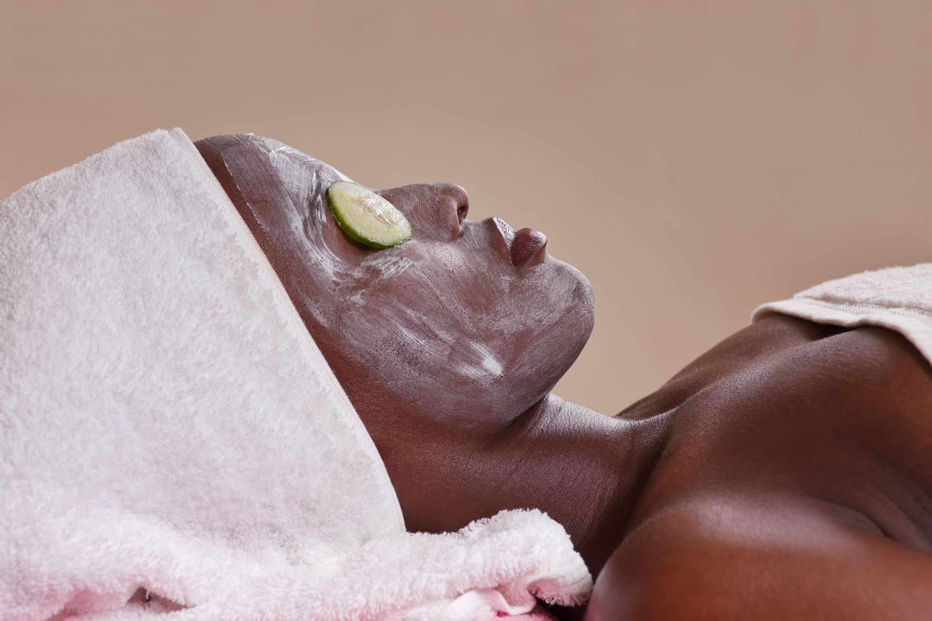 Person with facial mask, a towel on head, and a lime slice on eye, in a spa setting.