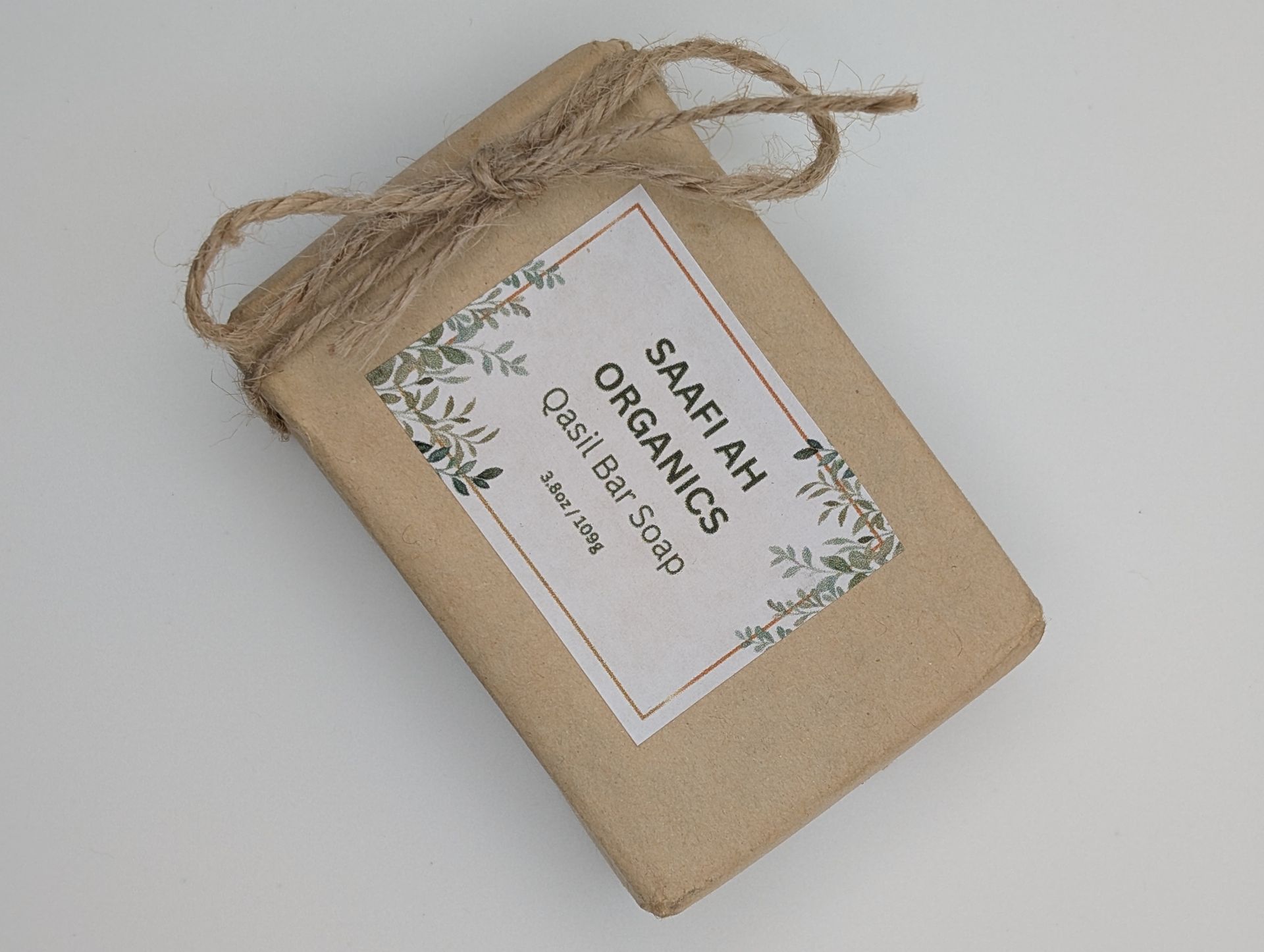 A bar of Saafiah Organics Qasil soap wrapped in brown paper and tied with twine against a plain white background.