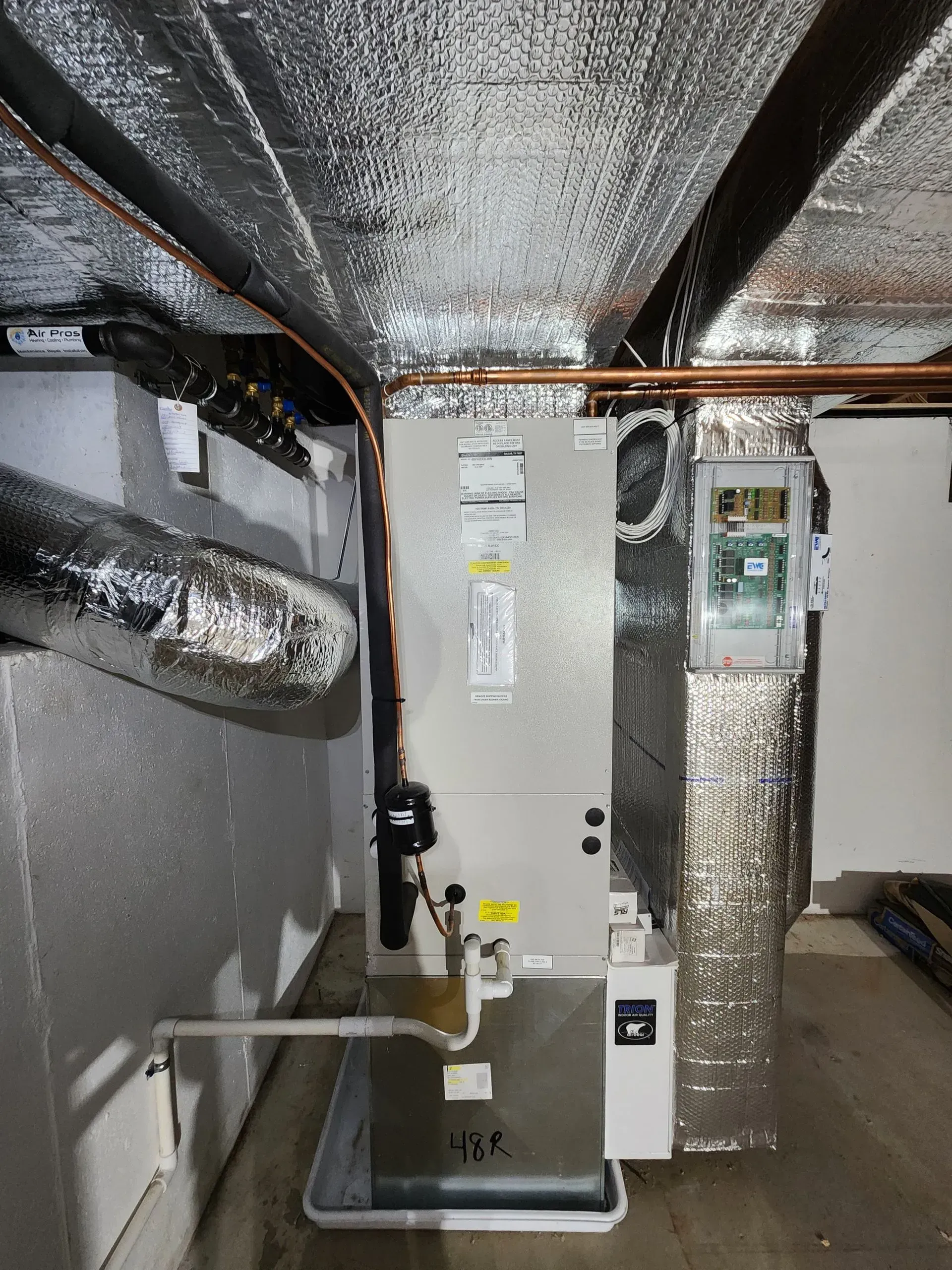 HVAC unit in a basement, with silver foil insulation on the ceiling and walls. Copper pipes and ductwork visible.