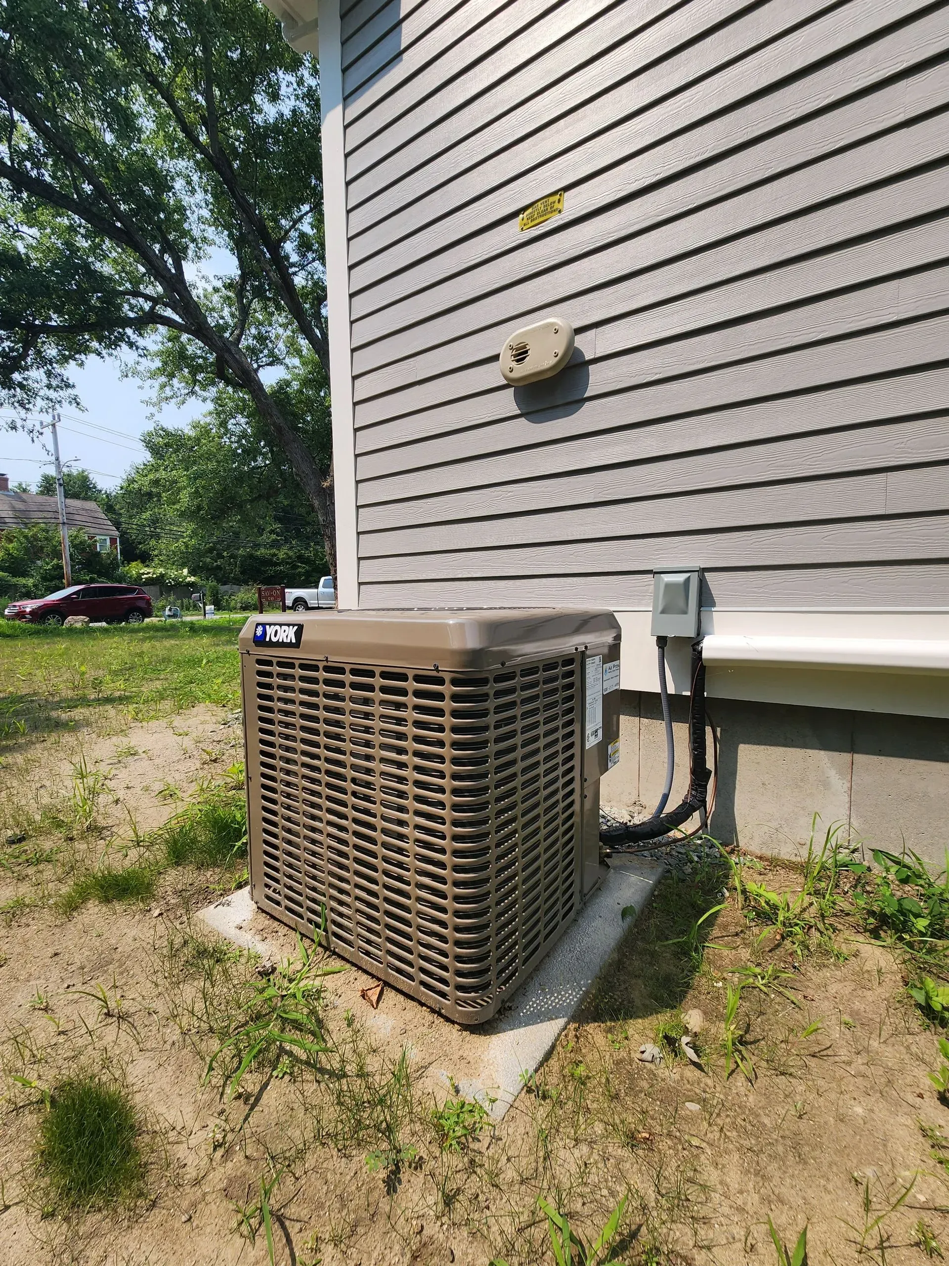 Air conditioning unit outside a gray-sided building, set on a concrete pad, on a grassy plot.