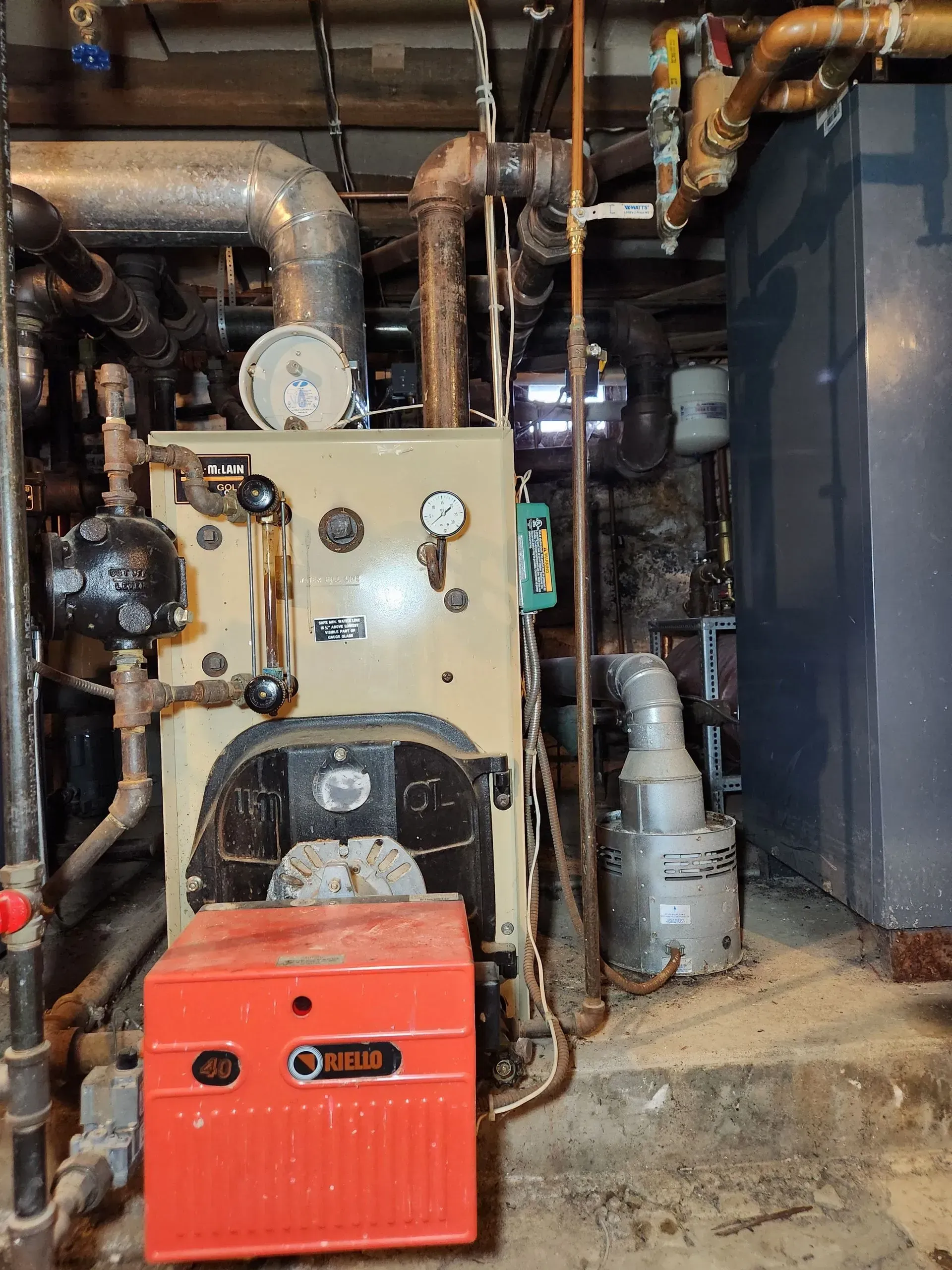 Oil furnace with red control box, pipes, gauges, and a gray tank in a basement.