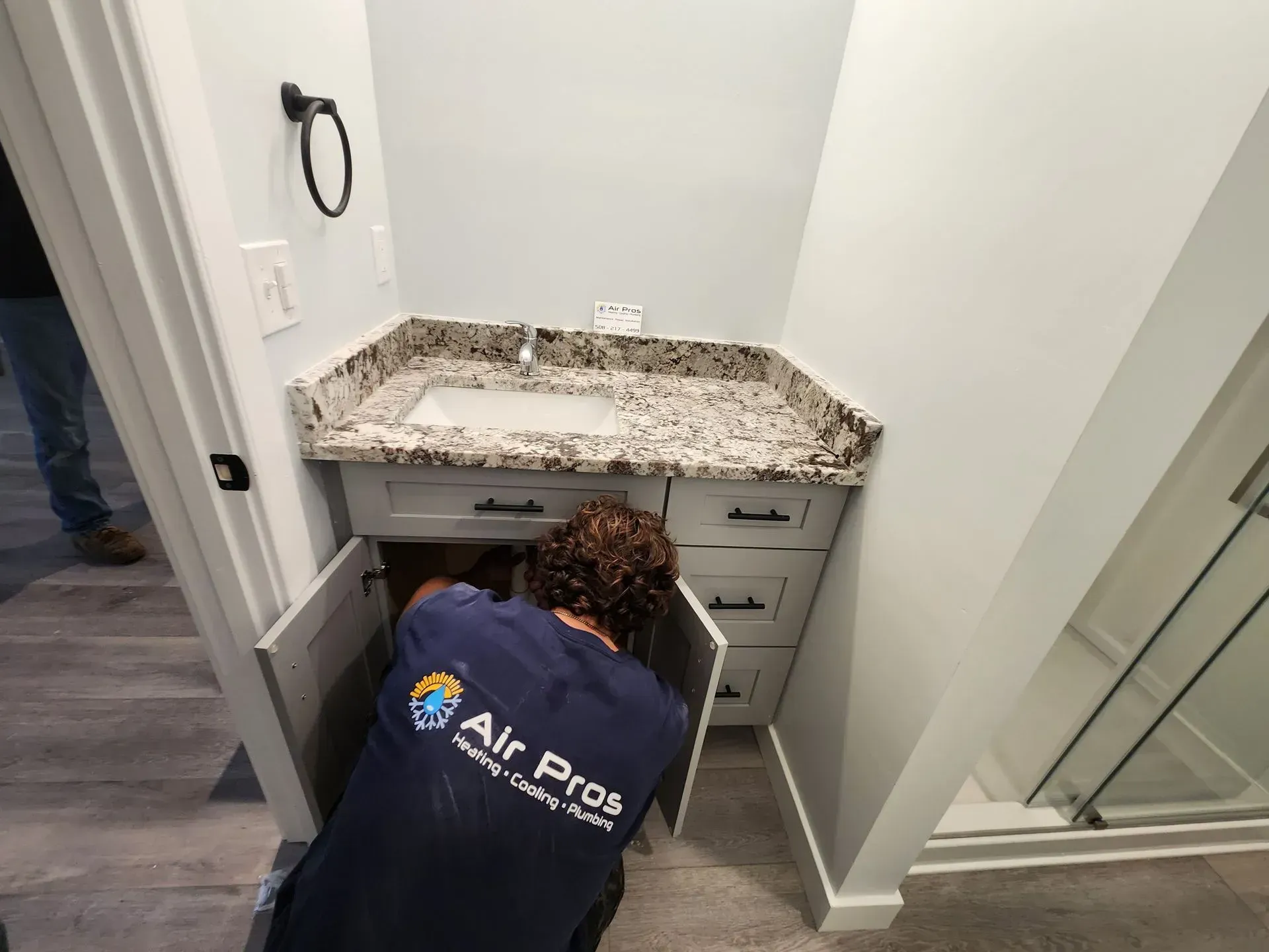 Person working under a bathroom sink, in front of a countertop, white cabinets and blue walls.