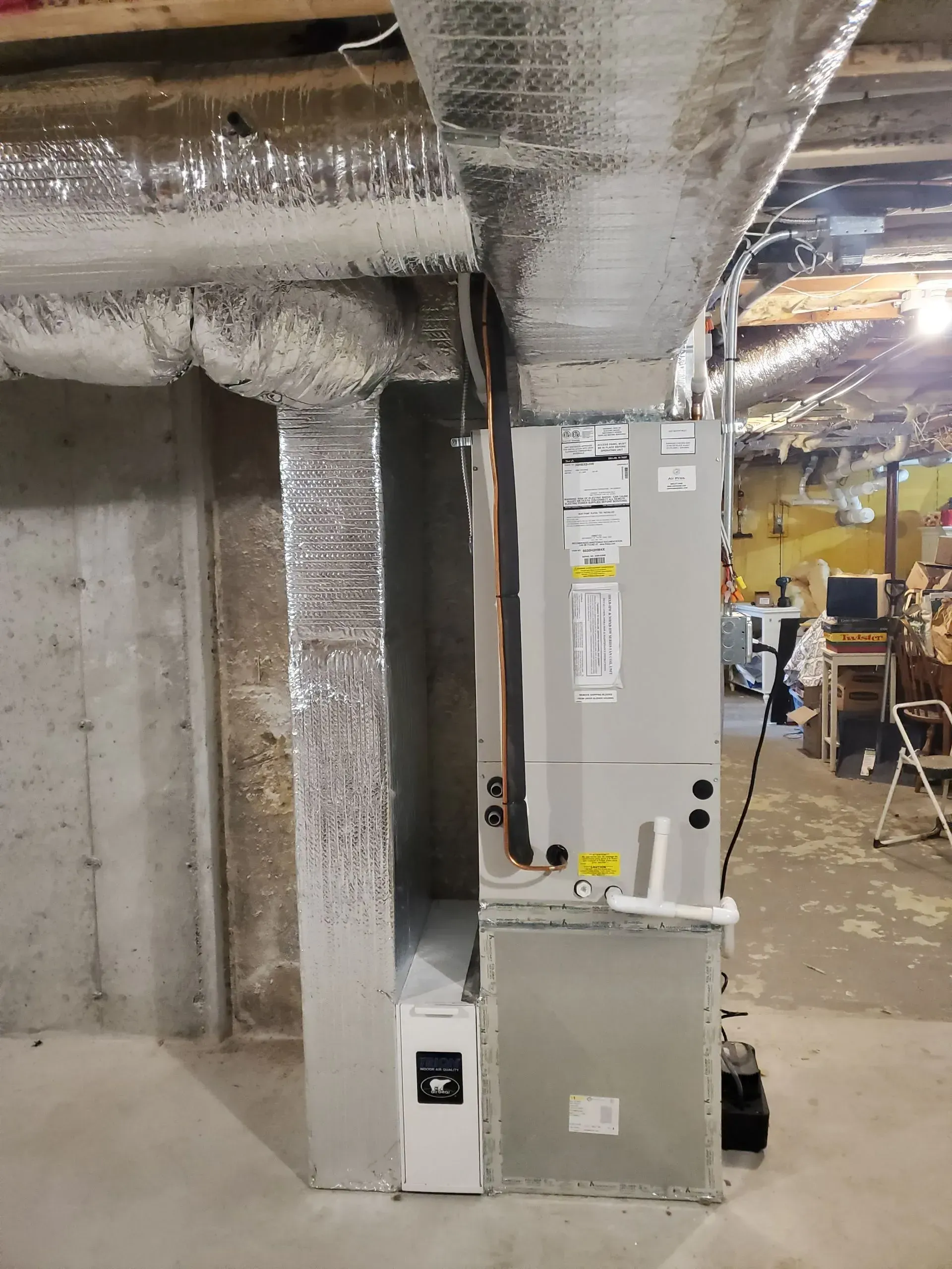 HVAC system in a basement setting with ductwork, gray unit, and concrete walls.