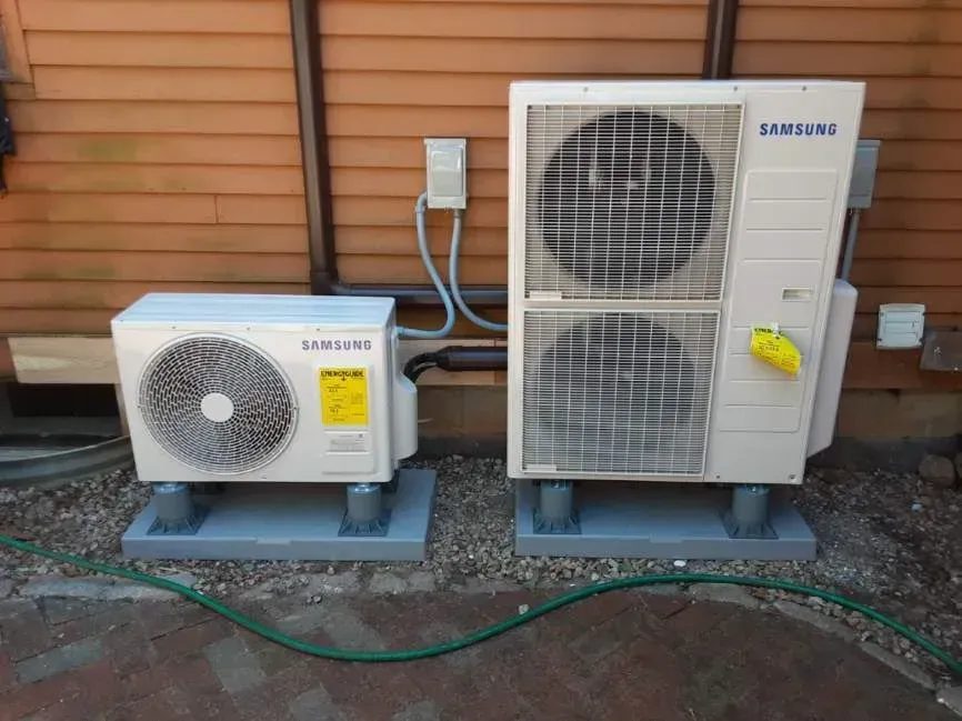 Two Samsung air conditioning units on concrete pads next to a brown building.