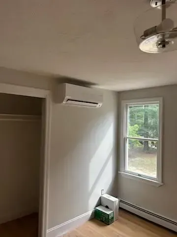 Air conditioning unit mounted on a light gray wall in a room with a closet and a window.