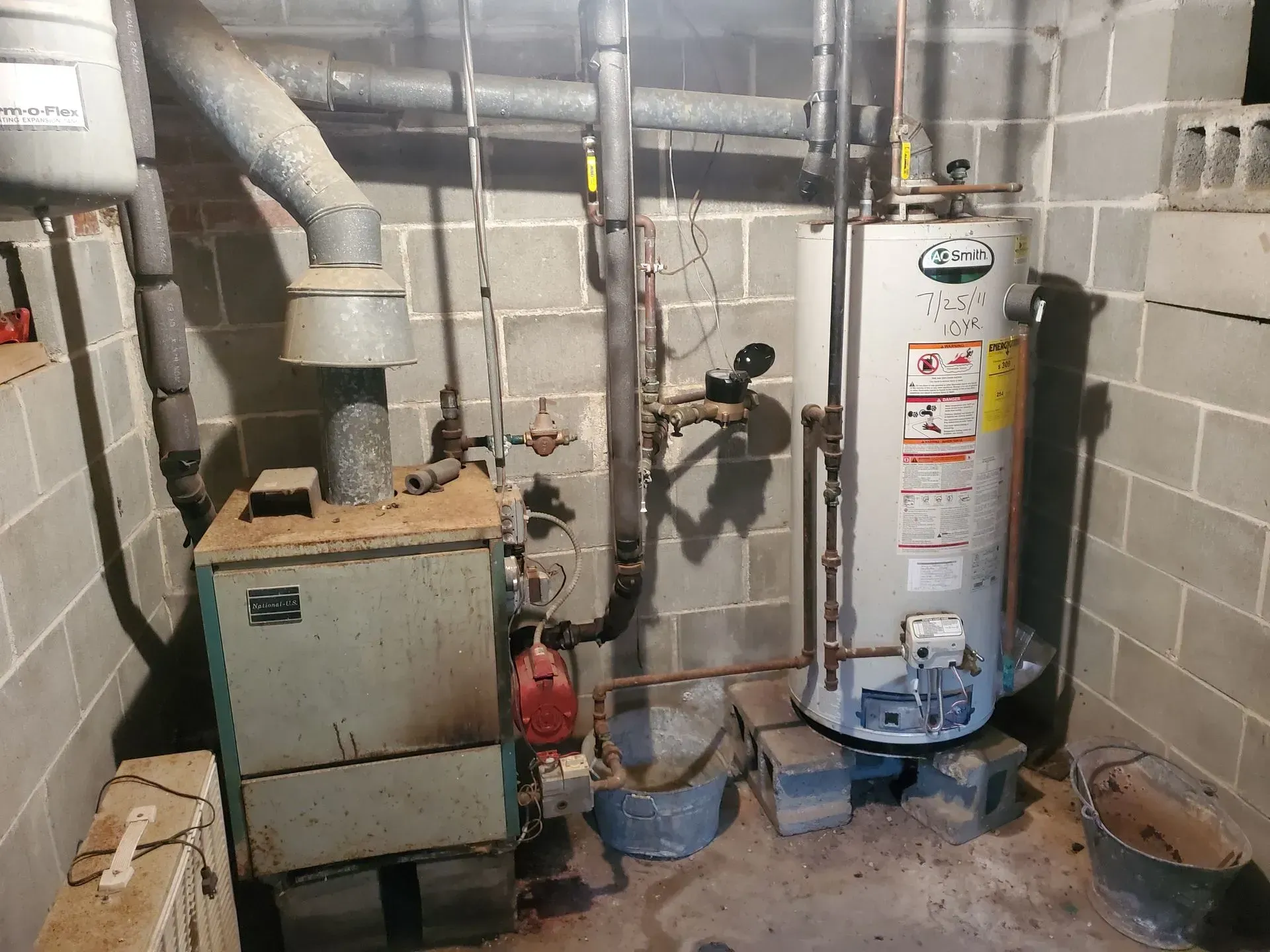 A basement with a furnace, water heater, and related pipes. Concrete block walls and floor.