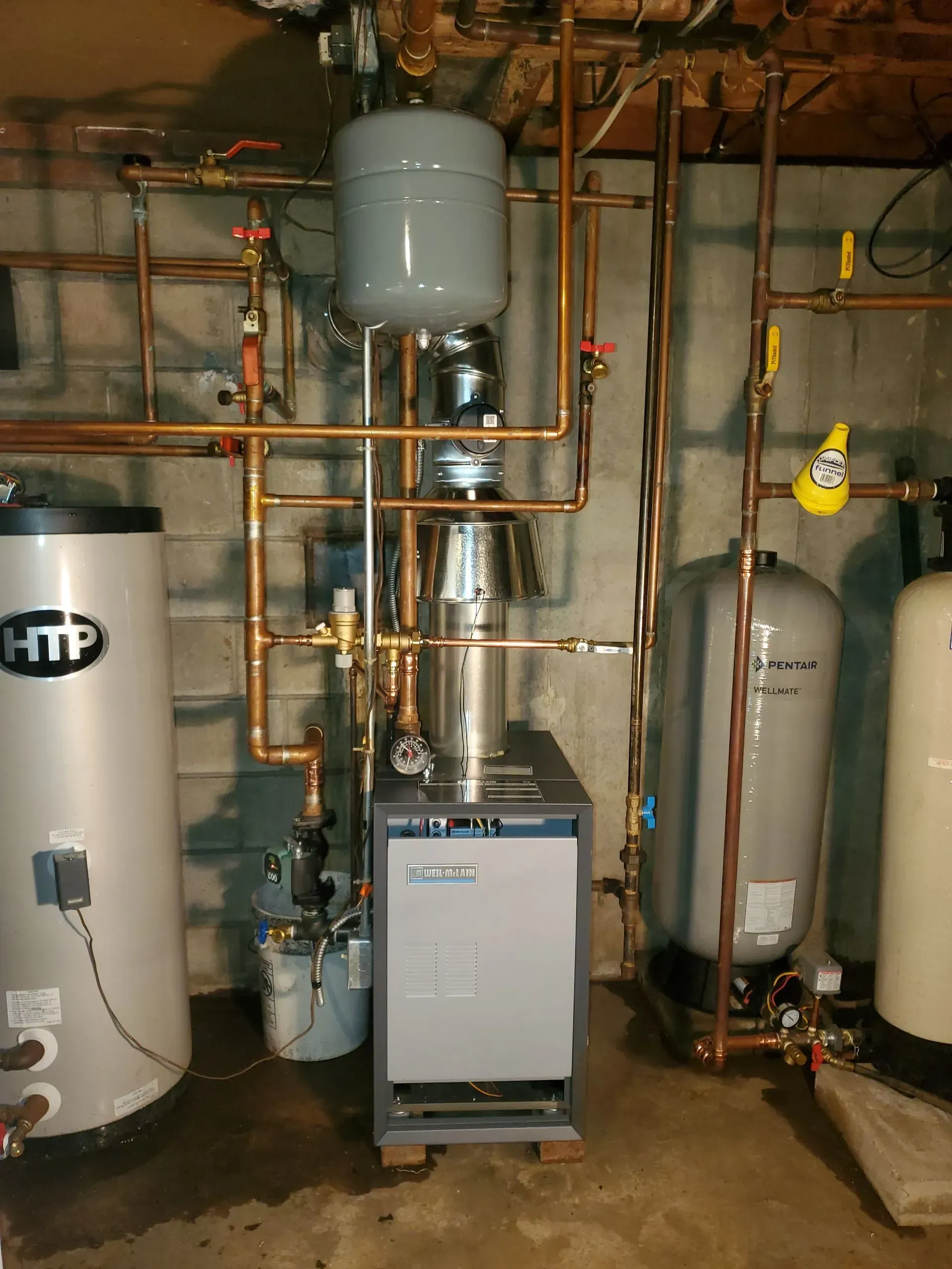 Plumbing system with boiler, tanks, and copper pipes in a basement. Grey, copper, and silver colors.