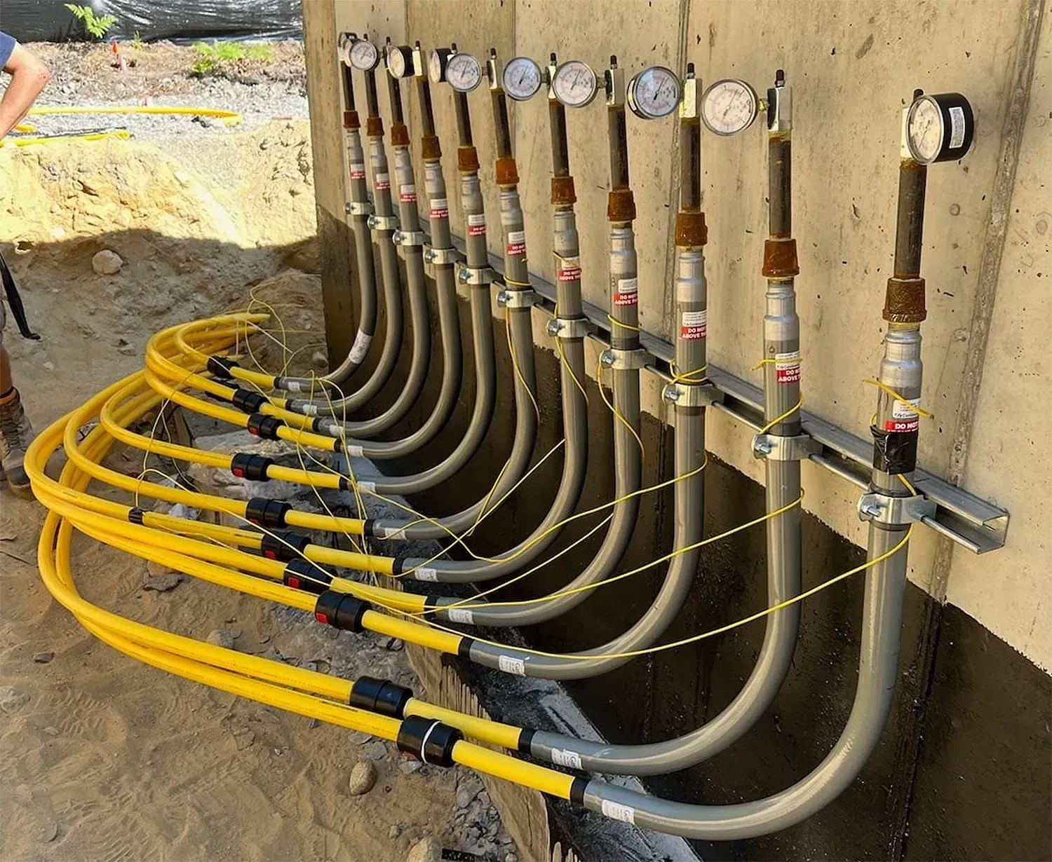 Yellow gas pipes and grey metal tubes with gauges attached to concrete wall.