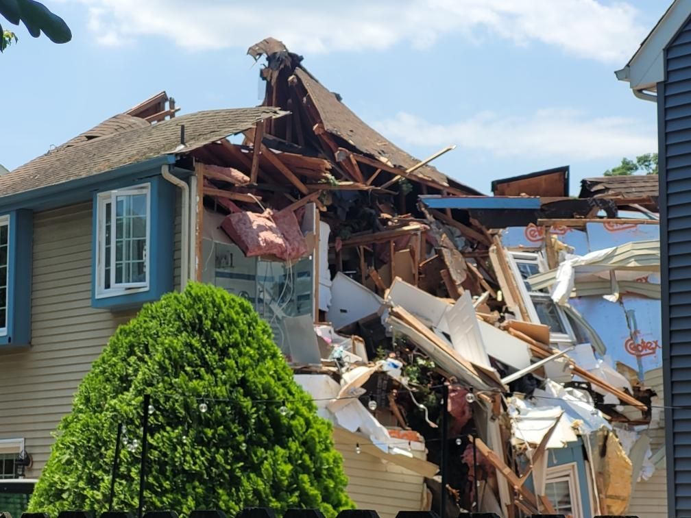 House severely damaged, with roof and walls partially collapsed, blue sky.
