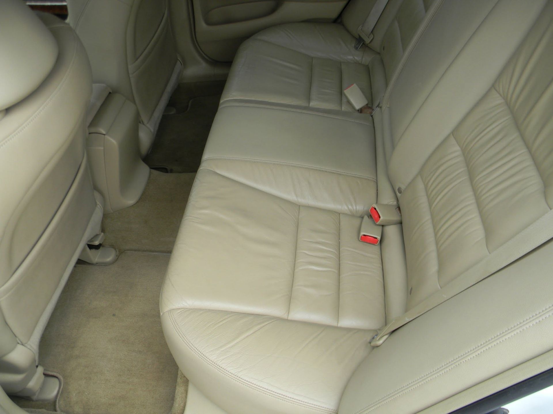 Beige leather back seat of a car interior, with red seat belt buckles visible.