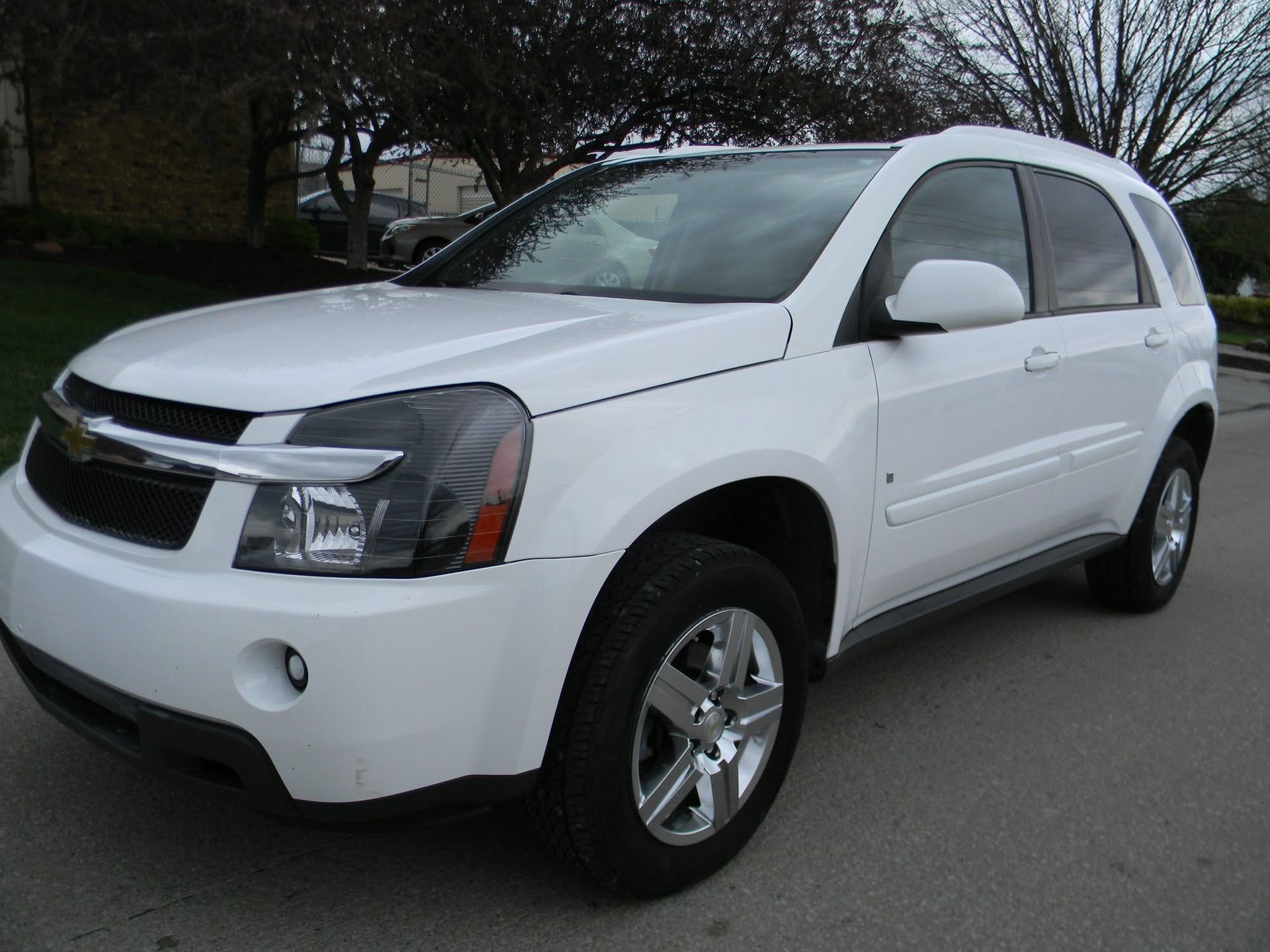 White SUV parked on a street, front-left view, with chrome wheels and trees in the background