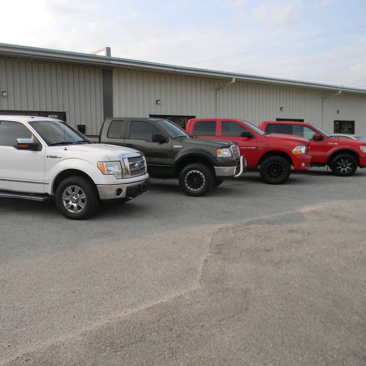 Four pickup trucks parked in a row outside a metal building.